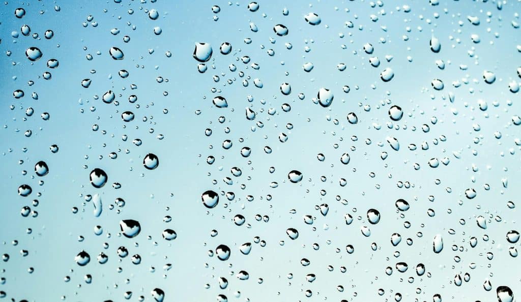 Close-up view of water droplets on glass against a blue sky background.